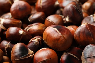 Photo of Pile of delicious edible roasted chestnuts as background, closeup