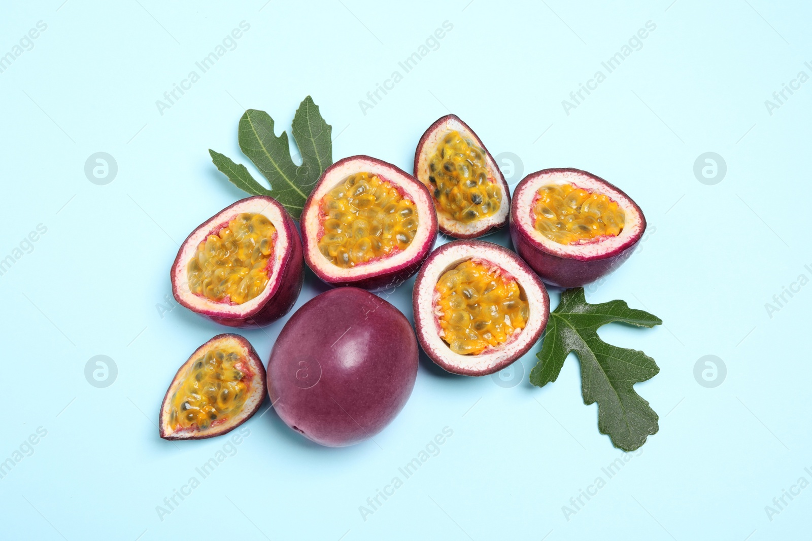 Photo of Fresh ripe passion fruits (maracuyas) with green leaves on light blue background, flat lay