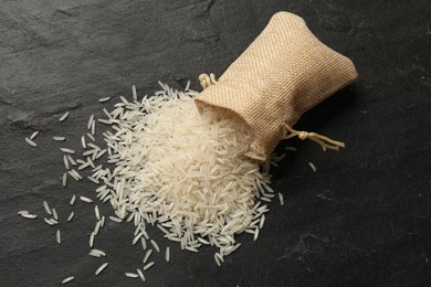 Photo of Raw basmati rice and overturned sack on black table, top view