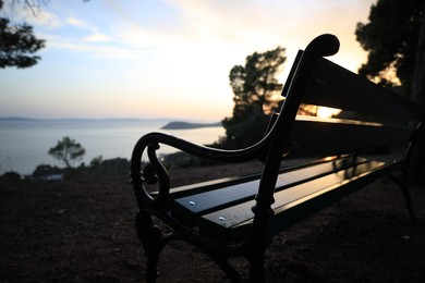 Photo of Wooden bench near seaside at sunset, selective focus. Space for text