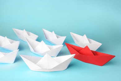 Photo of Group of paper boats following red one on light blue background. Leadership concept