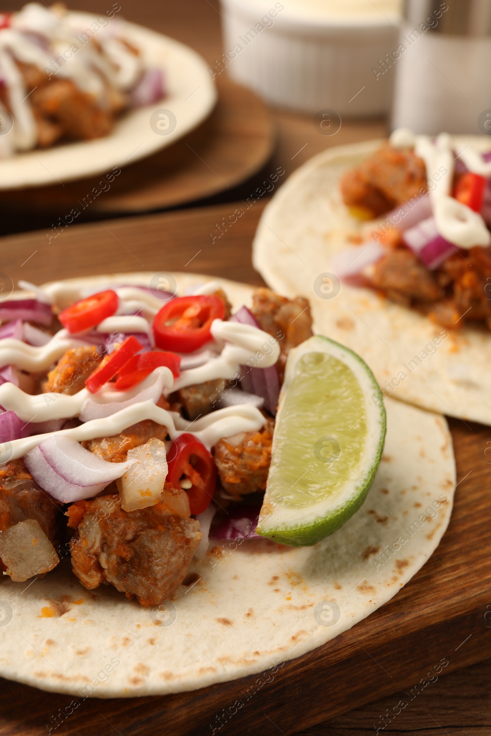 Photo of Delicious tacos with vegetables, meat and sauce on wooden table, closeup