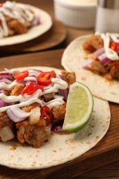 Photo of Delicious tacos with vegetables, meat and sauce on wooden table, closeup