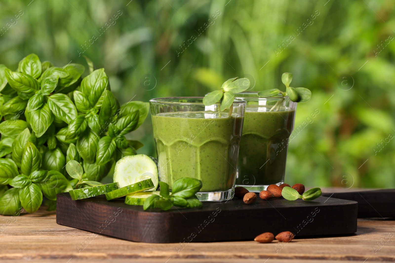 Photo of Glasses of fresh green smoothie and ingredients on wooden table outdoors