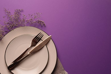 Stylish table setting. Plates, cutlery and floral decor on purple background, top view with space for text