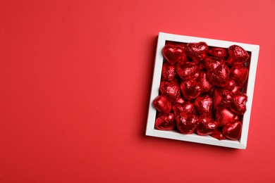 Photo of Tasty chocolate heart shaped candies in white box on red background, top view. Space for text