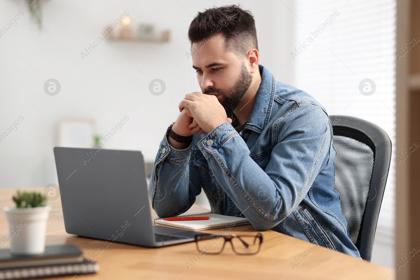 Photo of Young man watching webinar at table in room