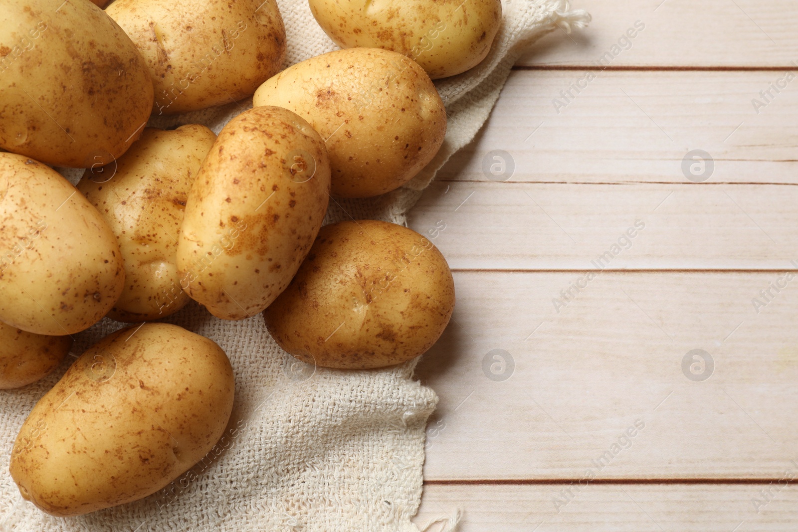 Photo of Raw fresh potatoes on light wooden table, top view. Space for text