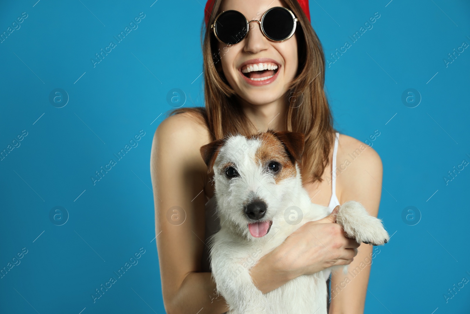 Photo of Young woman with her cute Jack Russell Terrier on light blue background. Lovely pet