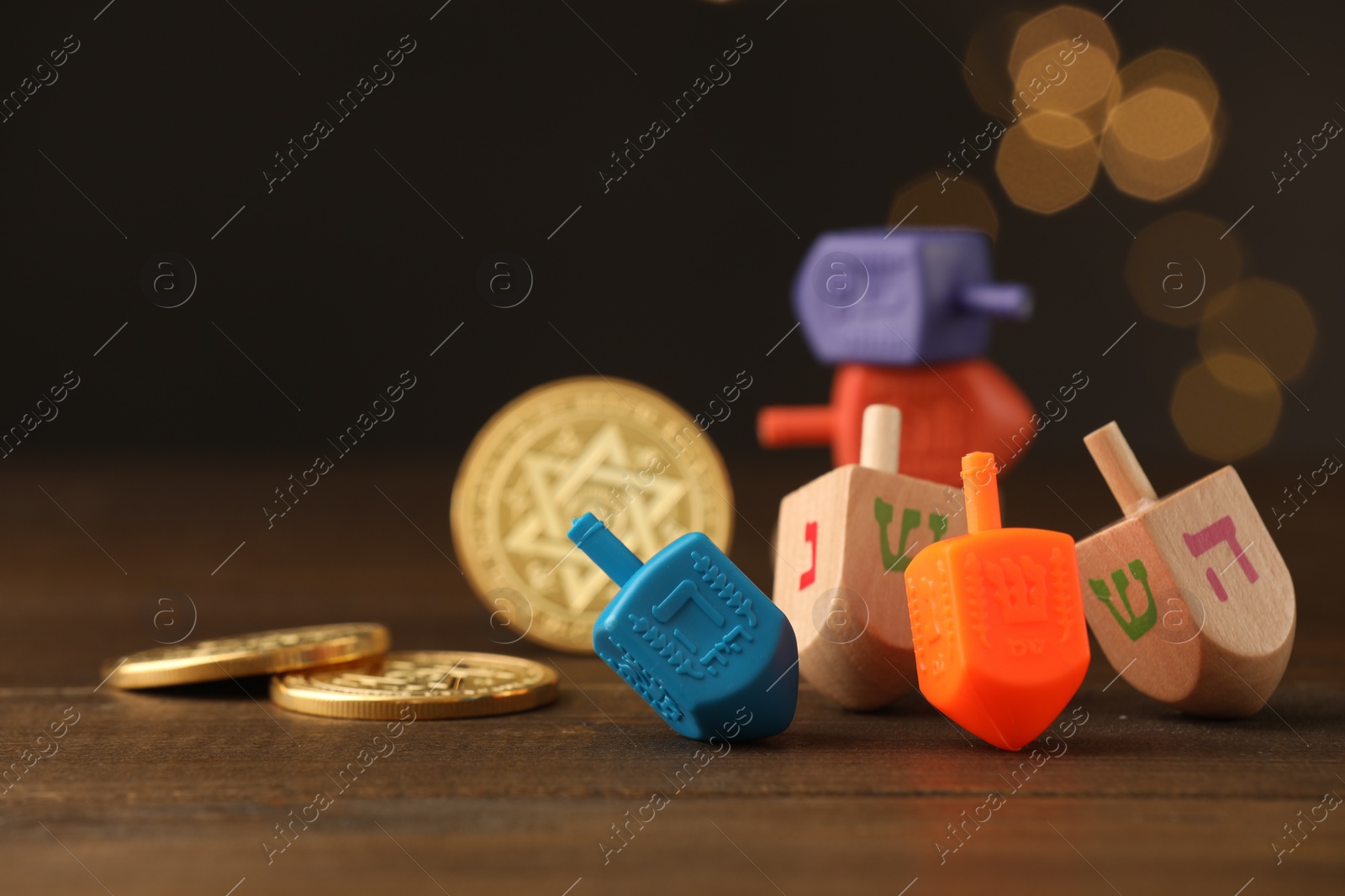 Photo of Dreidels with Jewish letters and coins on wooden table against blurred festive lights, selective focus. Space for text. Traditional Hanukkah game