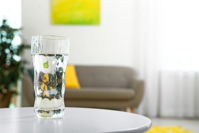 Glass of water on table in room, space for text. Refreshing drink