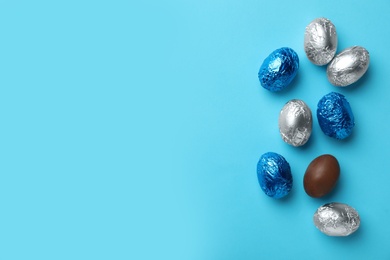 Photo of Chocolate eggs wrapped in colorful foil on light blue background, flat lay. Space for text