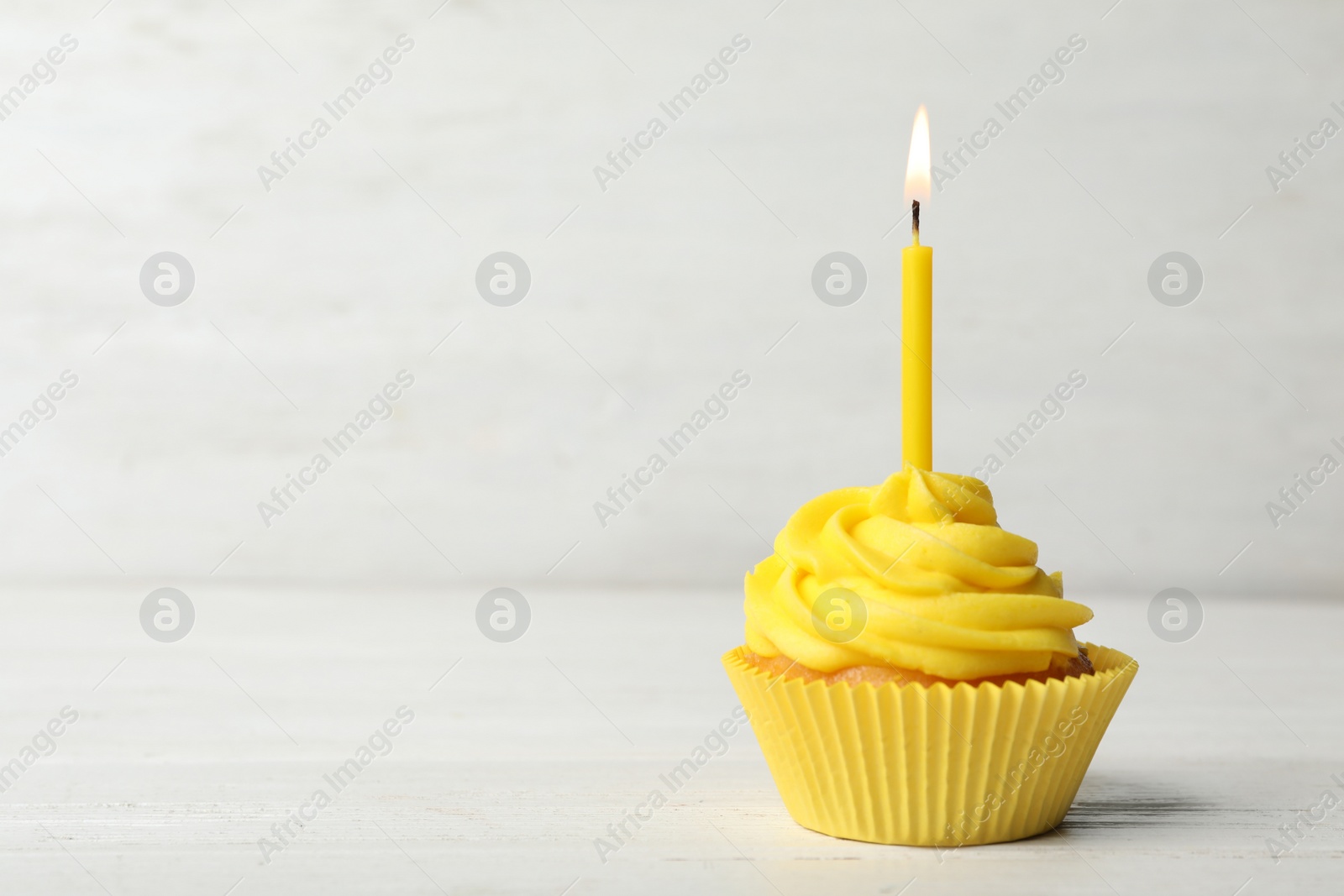 Photo of Delicious birthday cupcake with cream and burning candle on white wooden table. Space for text