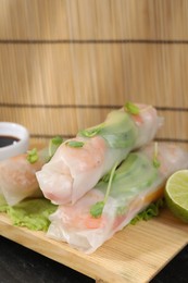 Photo of Delicious spring rolls, lettuce and lime on table