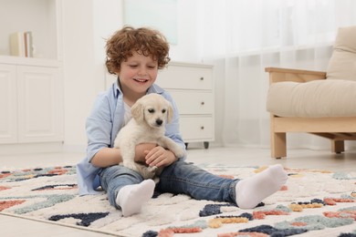 Photo of Little boy with cute puppy on carpet at home