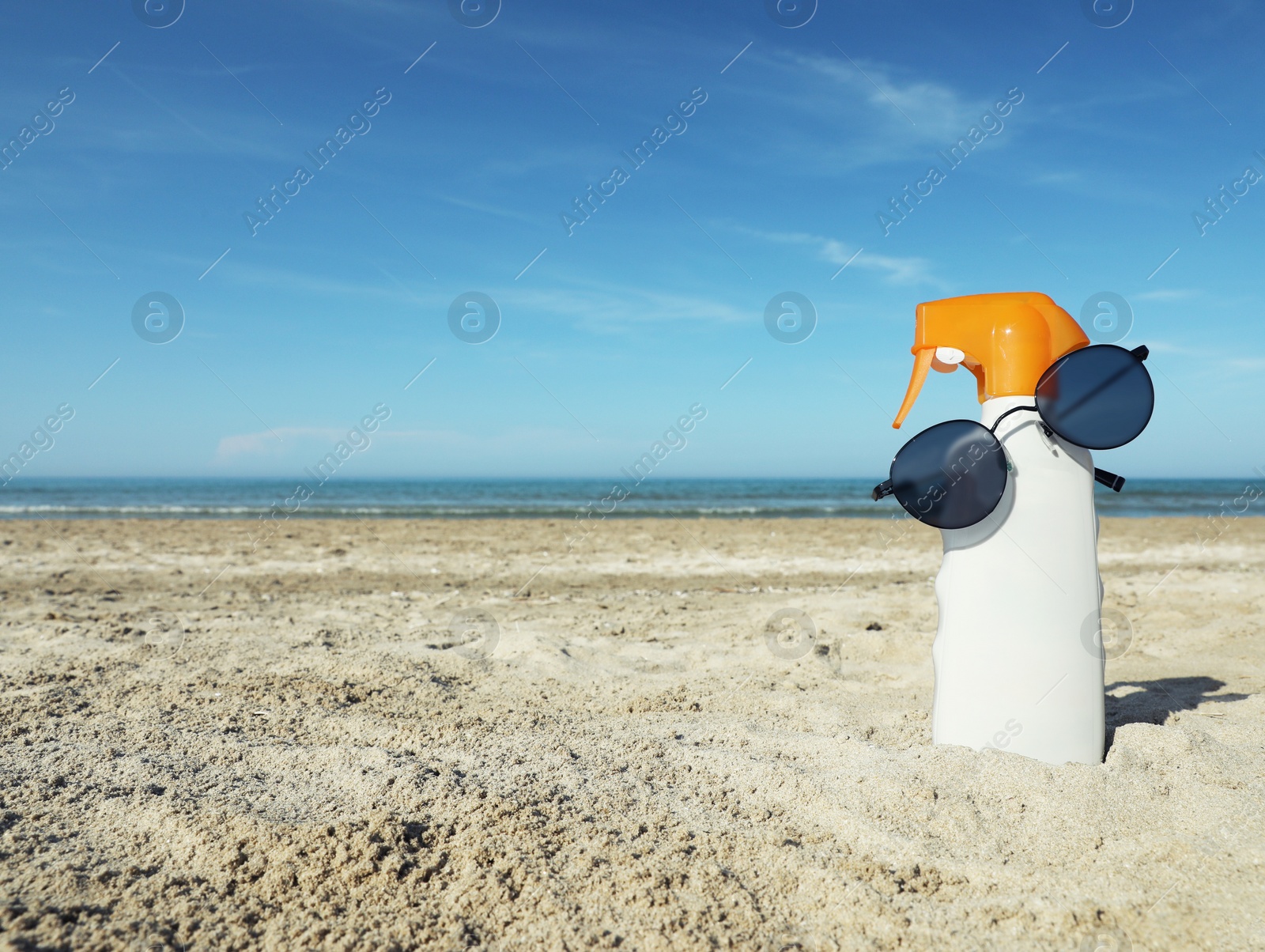 Photo of Bottle of sun protection product and sunglasses on sandy beach. Space for text