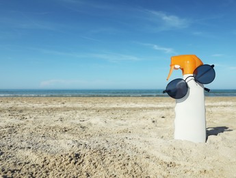 Bottle of sun protection product and sunglasses on sandy beach. Space for text