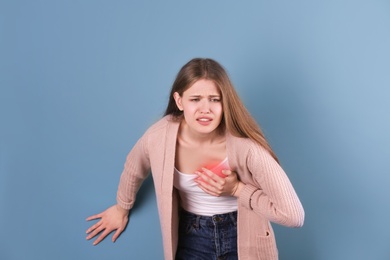 Young woman having heart attack on color background