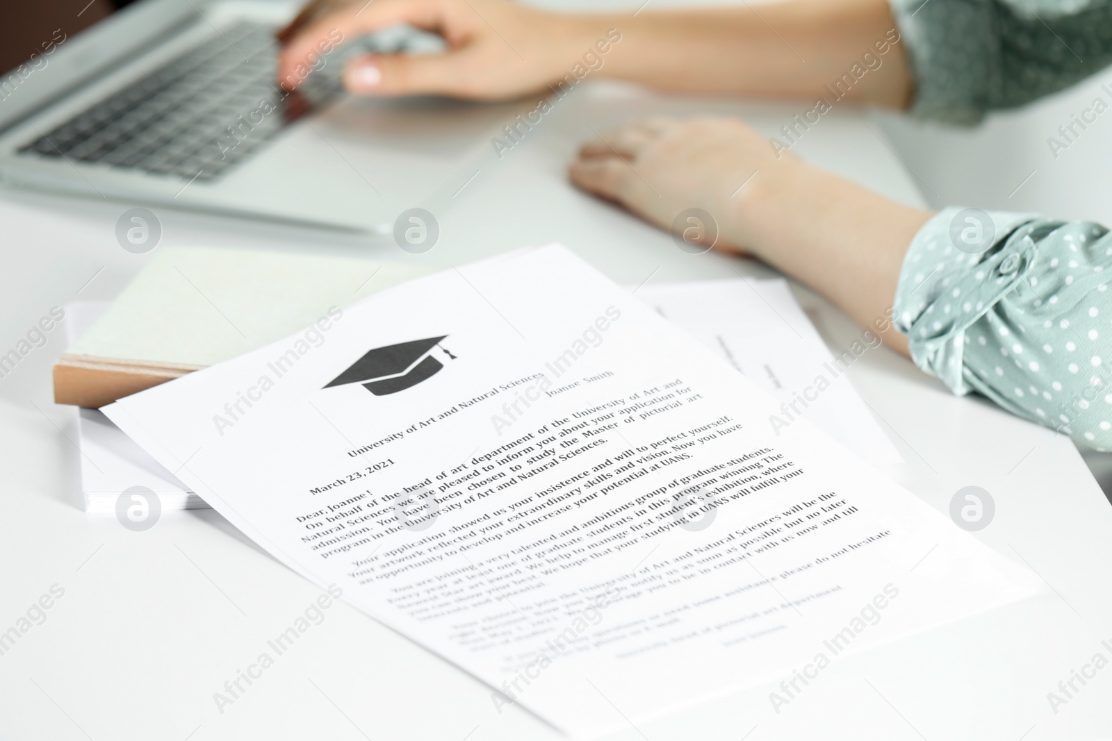 Photo of Student working with laptop at white table indoors, focus on acceptance letters from universities