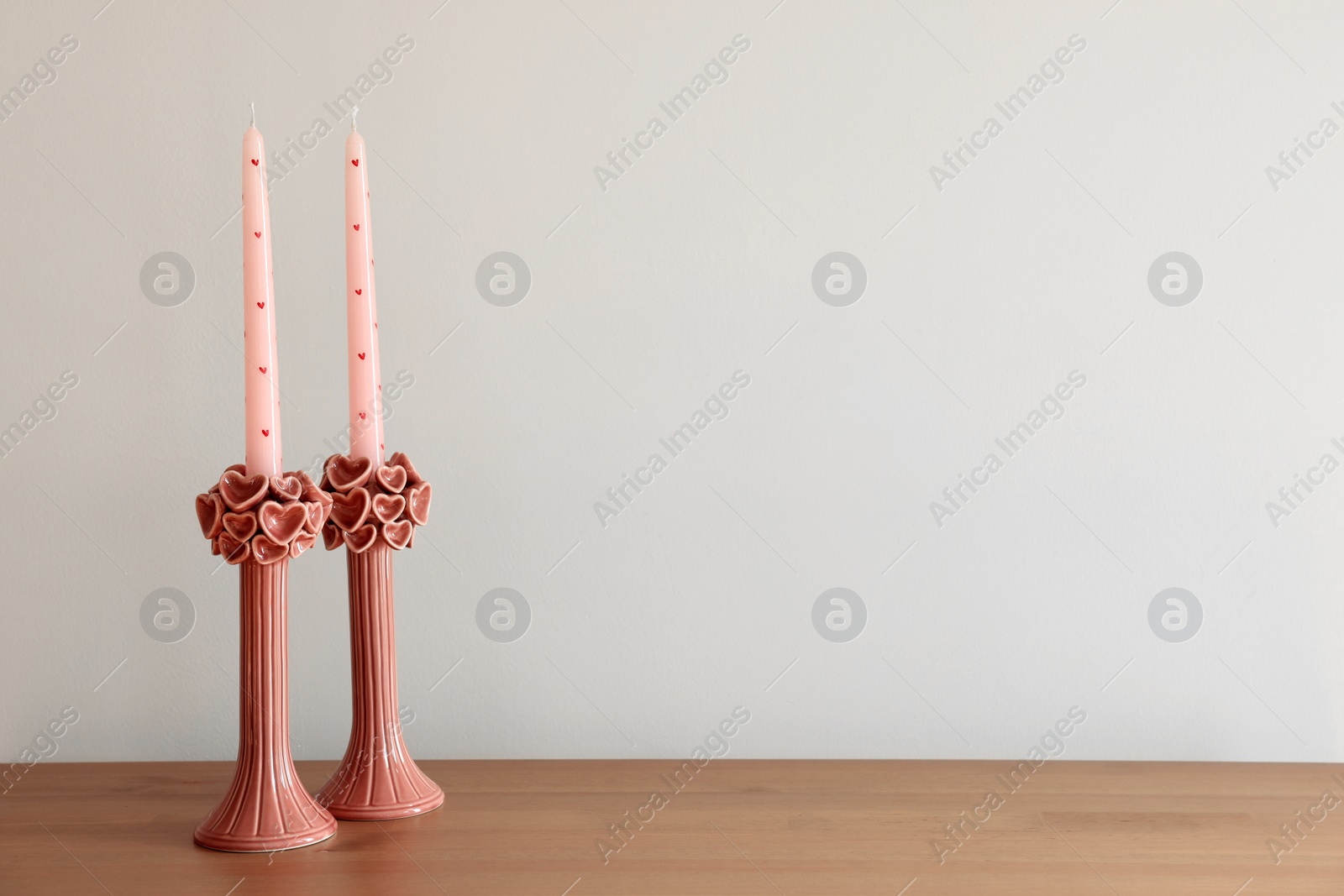 Photo of Beautiful pink candles on wooden table near white wall. Space for text