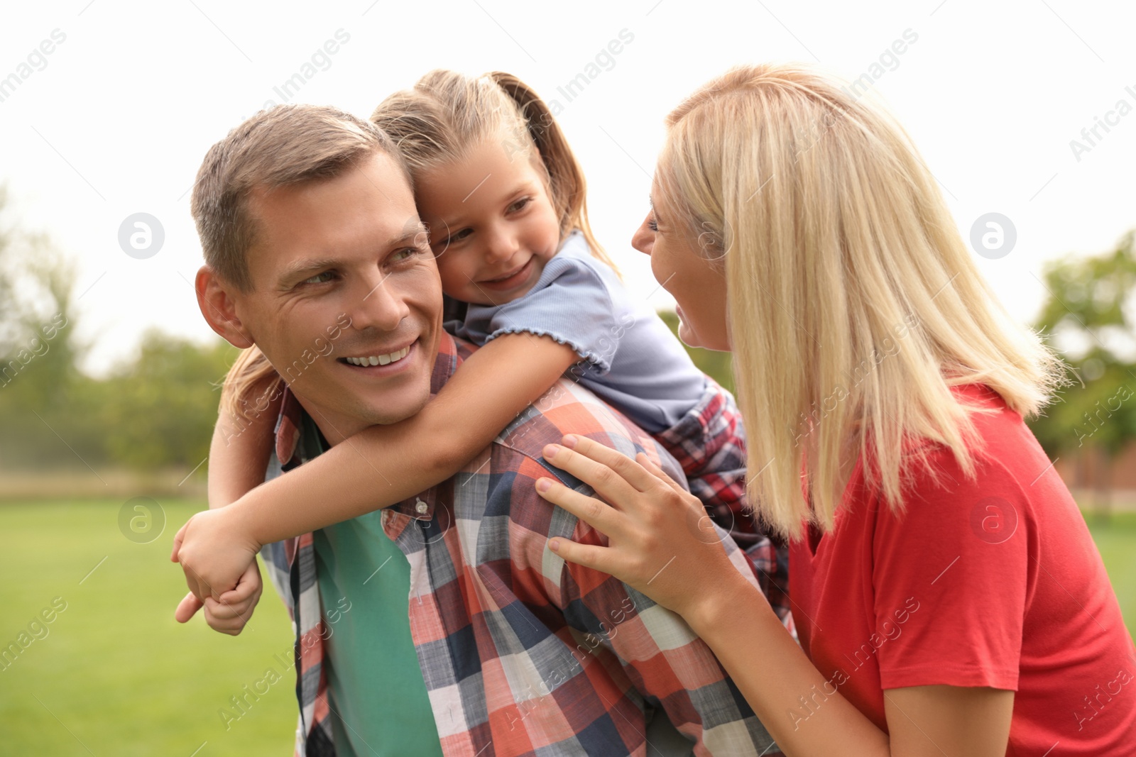 Photo of Cute little girl having fun with her parents in park on summer day