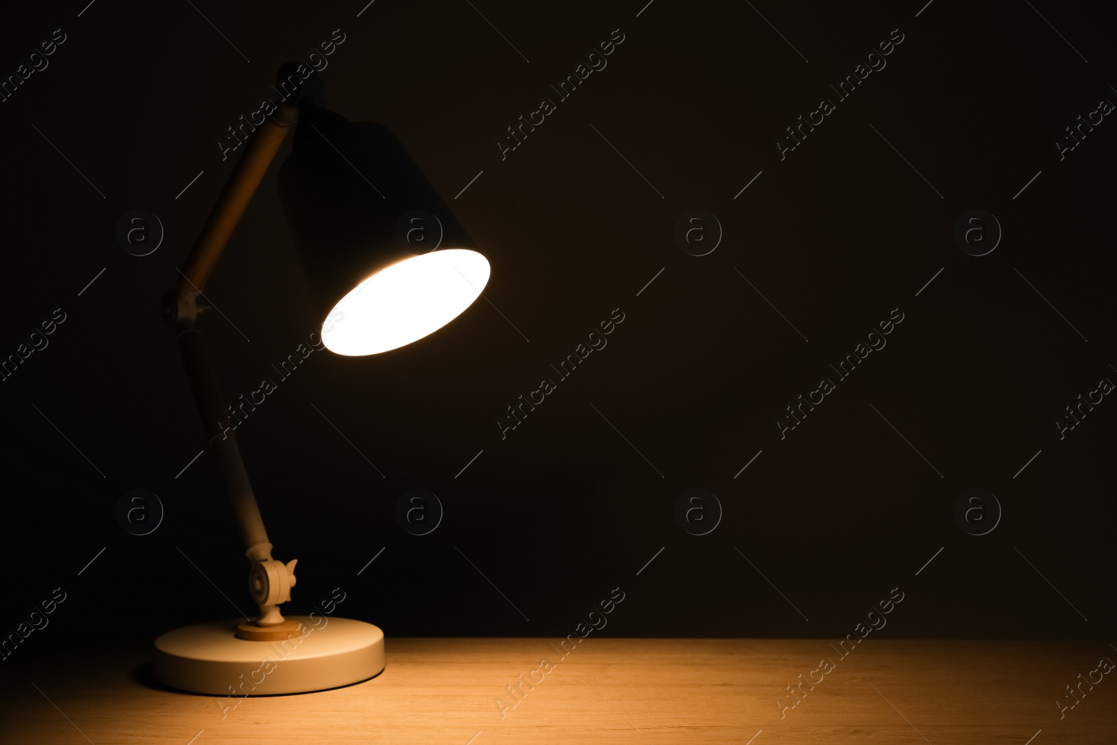 Photo of Stylish modern desk lamp on wooden table at night, space for text