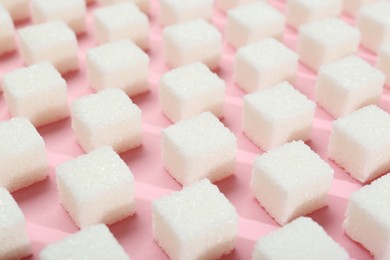 Photo of White sugar cubes on pink background, closeup