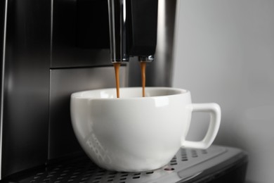 Photo of Espresso machine pouring coffee into cup against light background, closeup