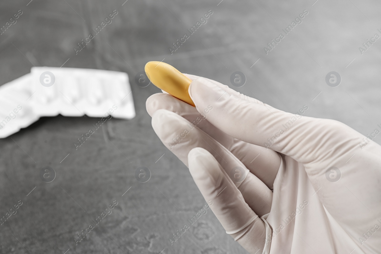 Photo of Woman holding suppository at grey table, closeup. Hemorrhoid treatment