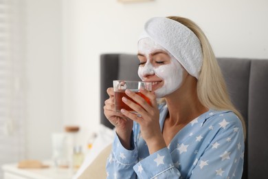Young woman with face mask drinking tea at home, space for text. Spa treatments