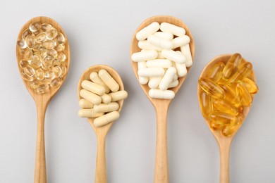 Photo of Wooden spoons with different vitamin capsules on light grey background, flat lay