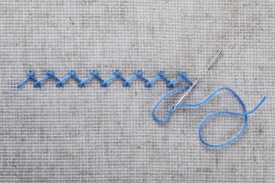 Photo of Embroidery stitches made with light blue thread and needle on canvas, top view