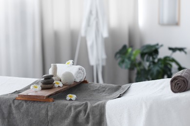 Photo of Stacked spa stones, flowers, herbal bags and towel on massage table in recreational center