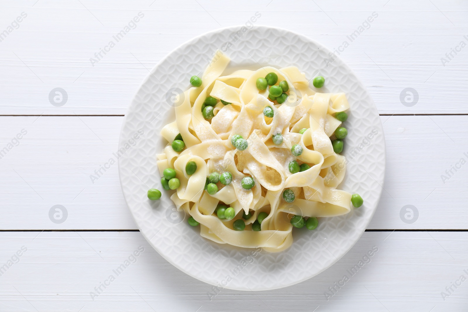 Photo of Delicious pasta with green peas on white wooden table, top view