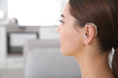 Young woman with hearing aid indoors, closeup. Space for text