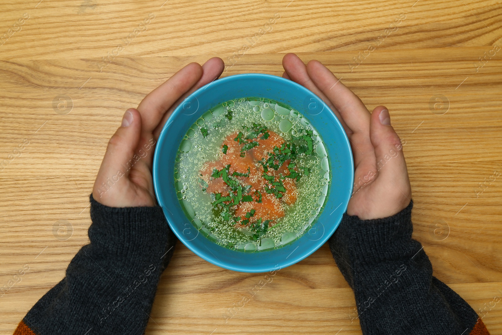 Photo of Man with bowl of soup at wooden table, top view. Flu treatment