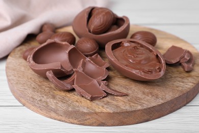 Photo of Broken and whole chocolate eggs with paste on white wooden table, closeup