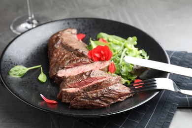Photo of Delicious grilled beef meat served with greens on grey table, closeup