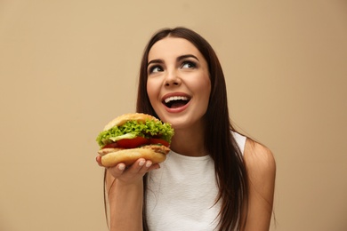 Young woman eating tasty burger on color background
