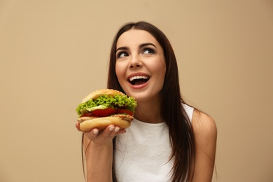 Photo of Young woman eating tasty burger on color background