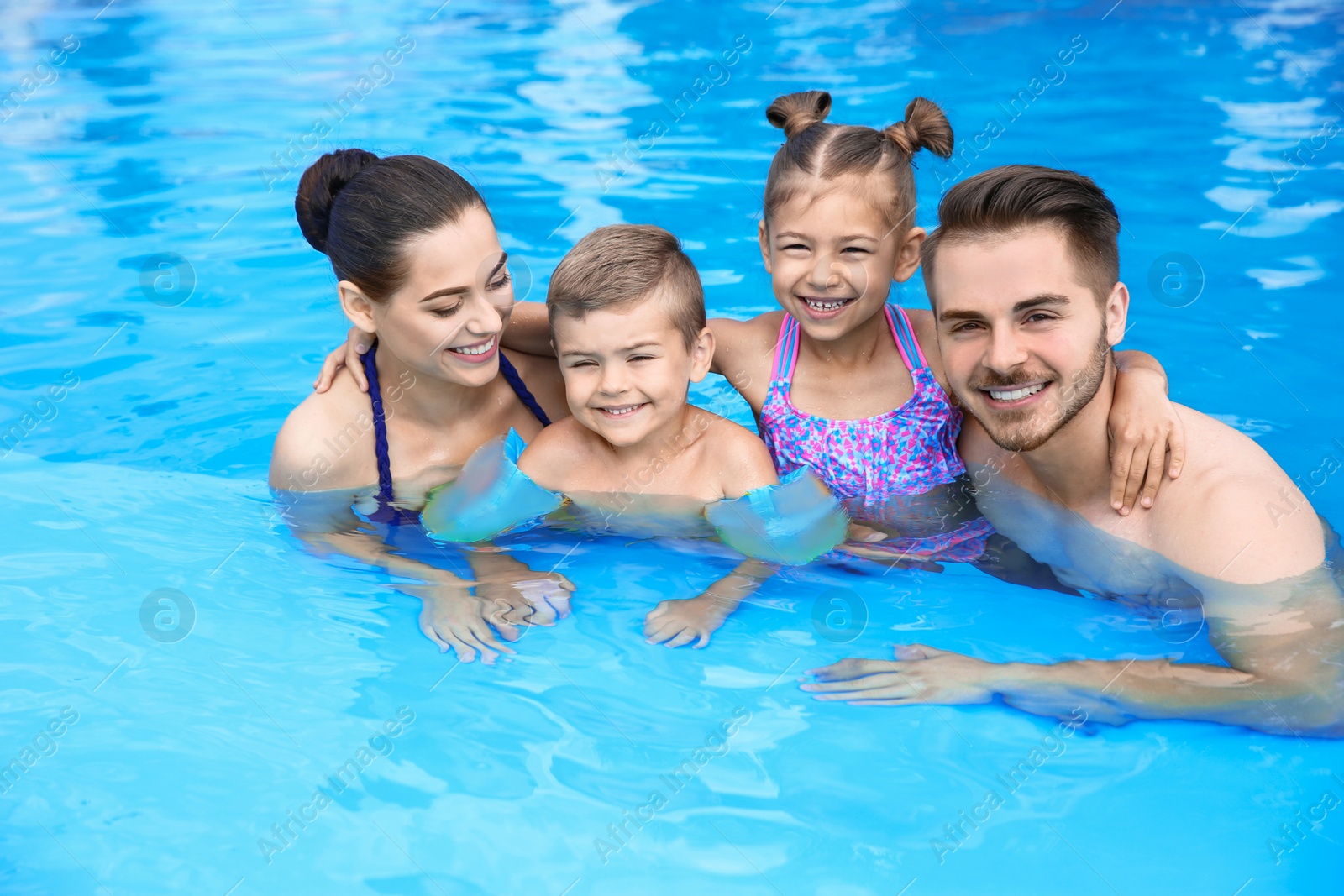 Photo of Young family with little children in swimming pool on sunny day