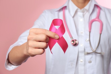 Female doctor with pink ribbon and stethoscope on color background, closeup. Breast cancer concept