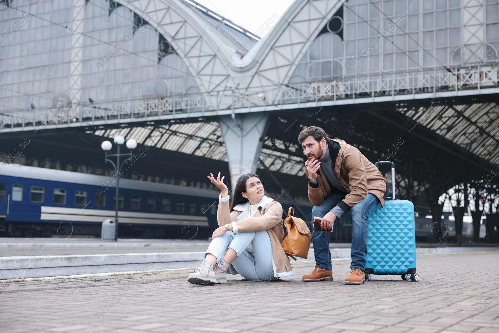 Photo of Being late. Worried couple with suitcase waiting at train station, space for text