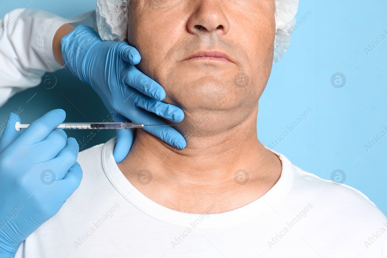 Photo of Mature man with double chin receiving injection on blue background, closeup