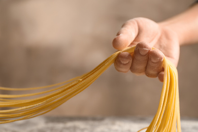 Photo of Woman holding noodles on light brown background, closeup. Italian pasta