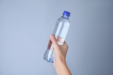 Woman holding plastic bottle with water on white background, closeup
