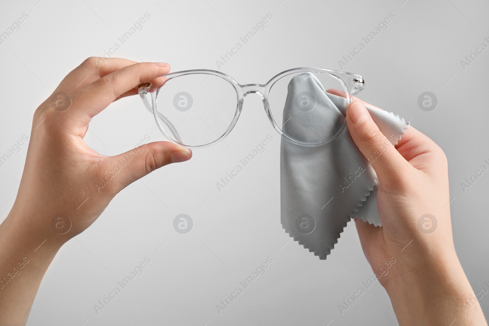 Photo of Woman wiping glasses with microfiber cloth on light grey background, closeup