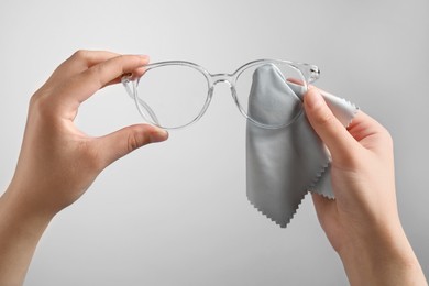 Photo of Woman wiping glasses with microfiber cloth on light grey background, closeup