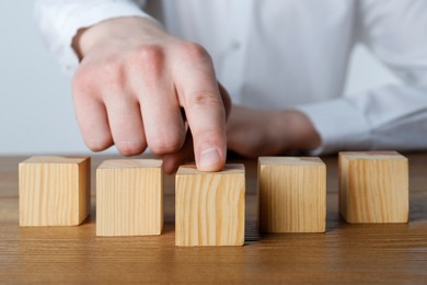 Photo of Man arranging empty cubes in row on wooden table, closeup. Space for text
