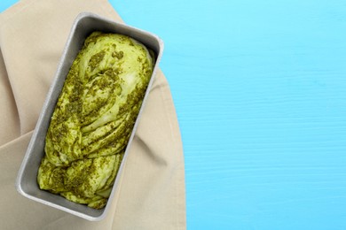 Photo of Uncooked pesto bread in baking dish on light blue wooden table, top view. Space for text